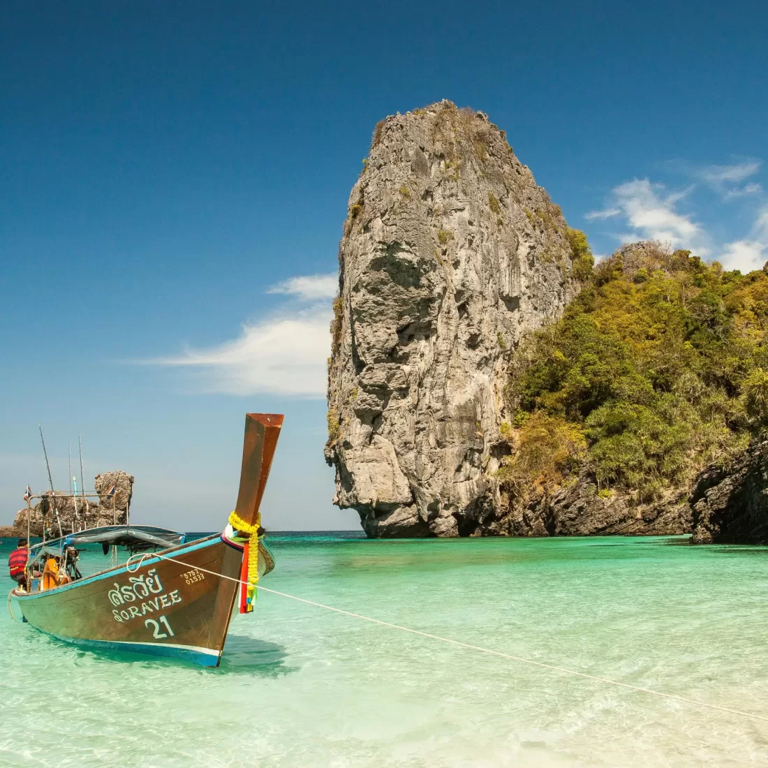A picturesque tropical beach with a traditional boat and stunning limestone cliffs in clear turquoise waters.