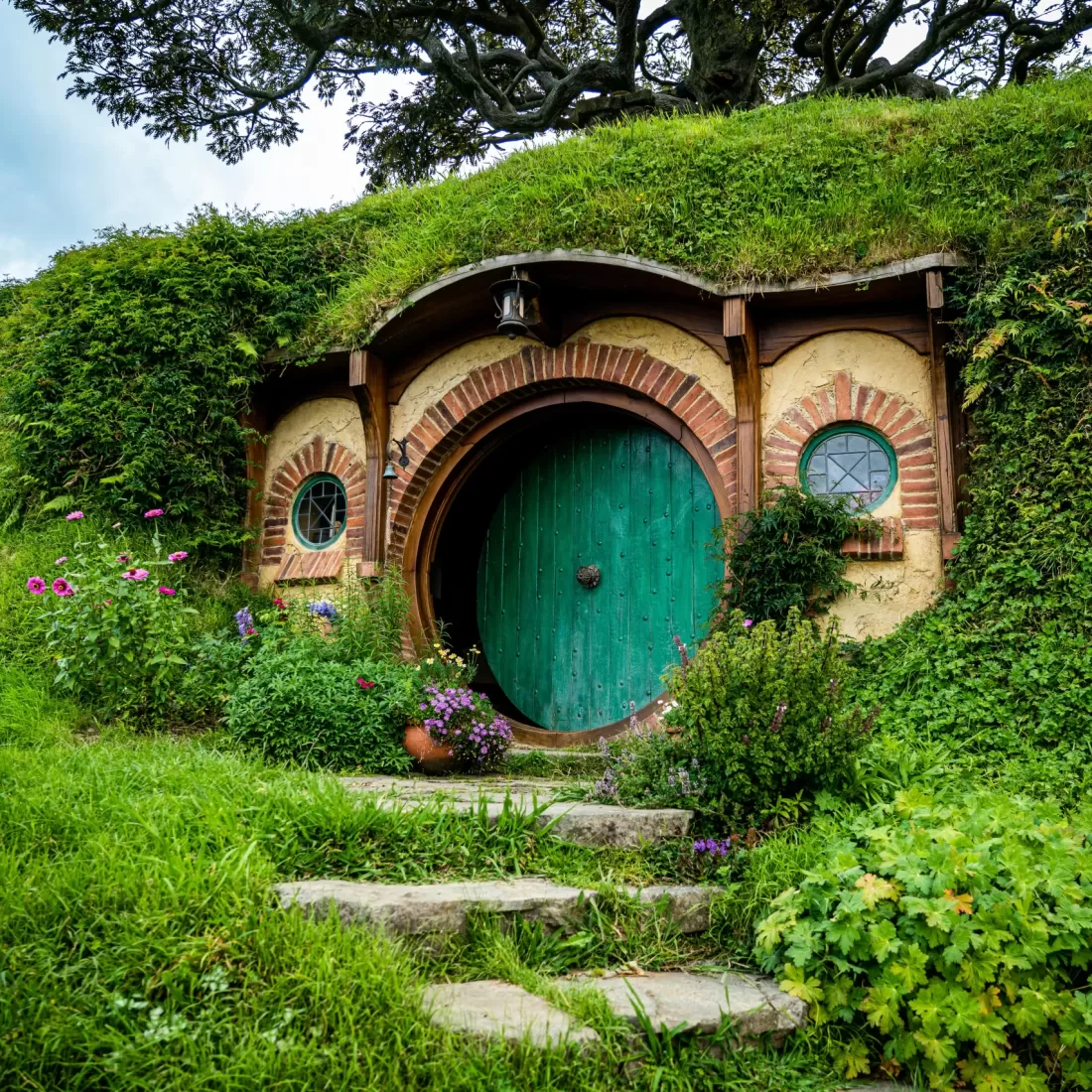 Picturesque Hobbiton house with a lush green roof and round door surrounded by vibrant garden.